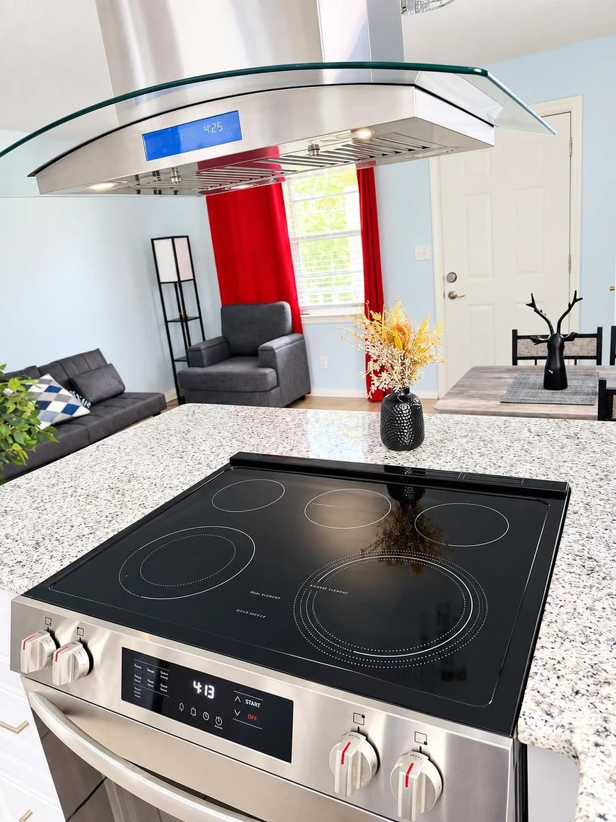 Kitchen island with a black glass cooktop, looking toward the living room and red curtains