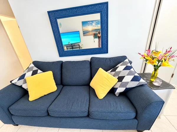 Navy sofa with yellow and patterned pillows beneath a blue-framed mirror