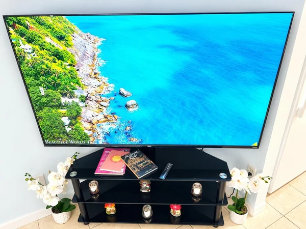 Large smart TV on a black media stand with white orchids