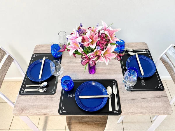 Dining table set for two with blue plates and a vase of pink lilies