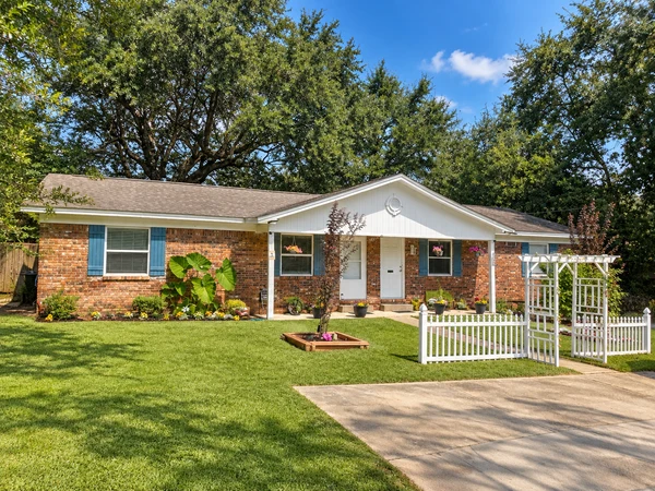 Front of the brick duplex with a driveway, picket fence and white arbor