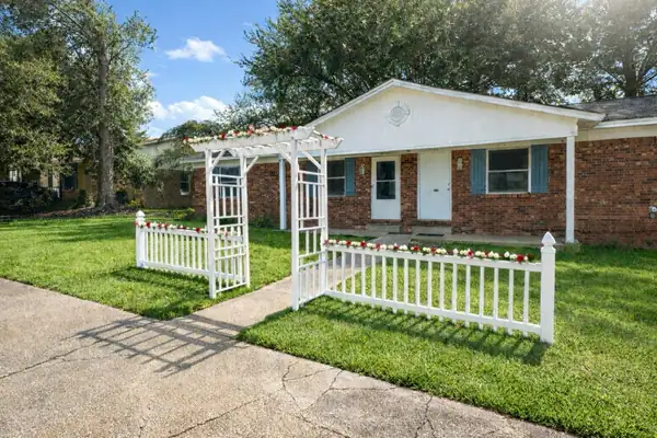 Brick ranch home behind a white picket fence and a flower-topped arbor